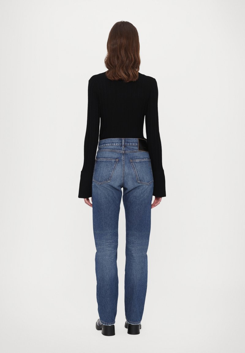 Haut noir à manches longues en côte associé à un jean droit bleu. Comprend une taille haute, cinq poches et une ceinture foncée.
