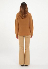 Pull marron côtelé à coupe décontractée et manches larges, associé à un pantalon beige évasé. Texture lisse, sans motifs ni accents visibles.
