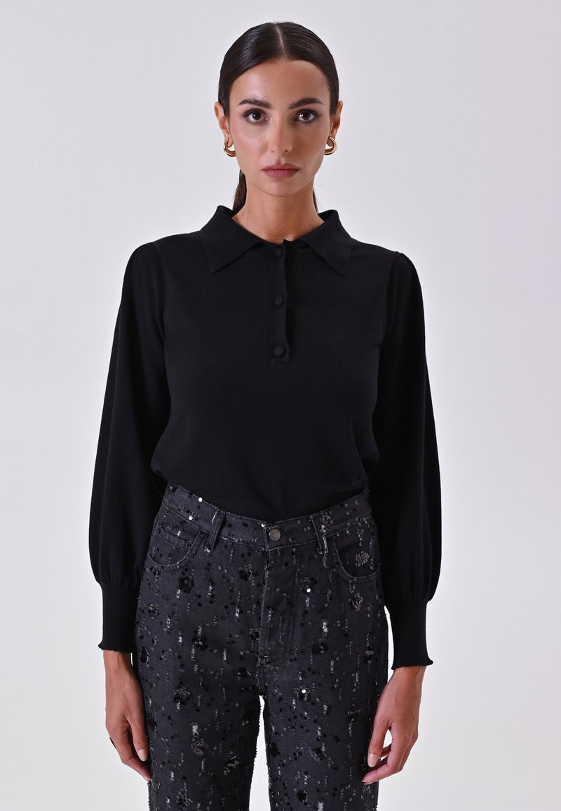 Polo a maniche lunghe nera con colletto e chiusura a bottoni, abbinata a jeans neri a vita alta con dettagli in paillettes e una finitura texture.