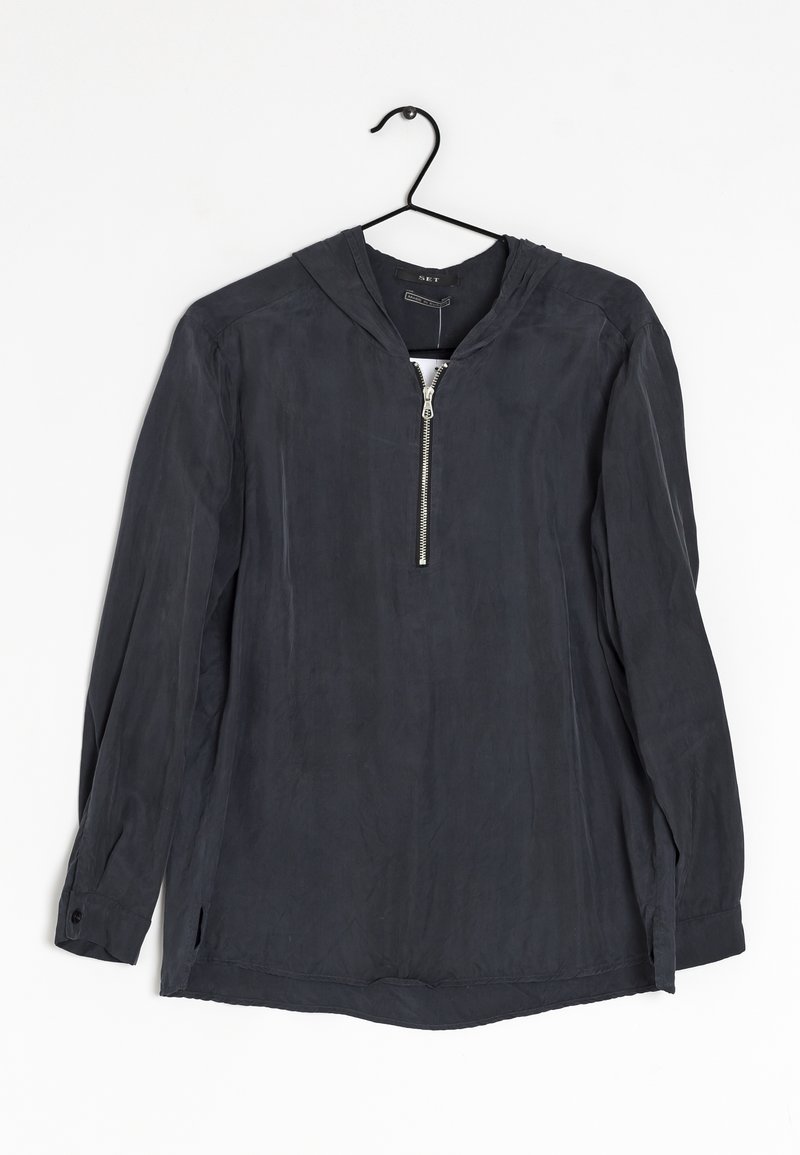 Chemise à capuche gris foncé à manches longues avec fermeture éclair à l'avant, suspendue à un cintre noir sur fond blanc.