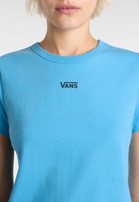Vaaleansininen puuvillat-paita, jossa on pyöreä kaula-aukko ja lyhyet hihat, ja jossa on musta "VANS" -logo painettuna rintaan. Pehmeä tekstuuri.