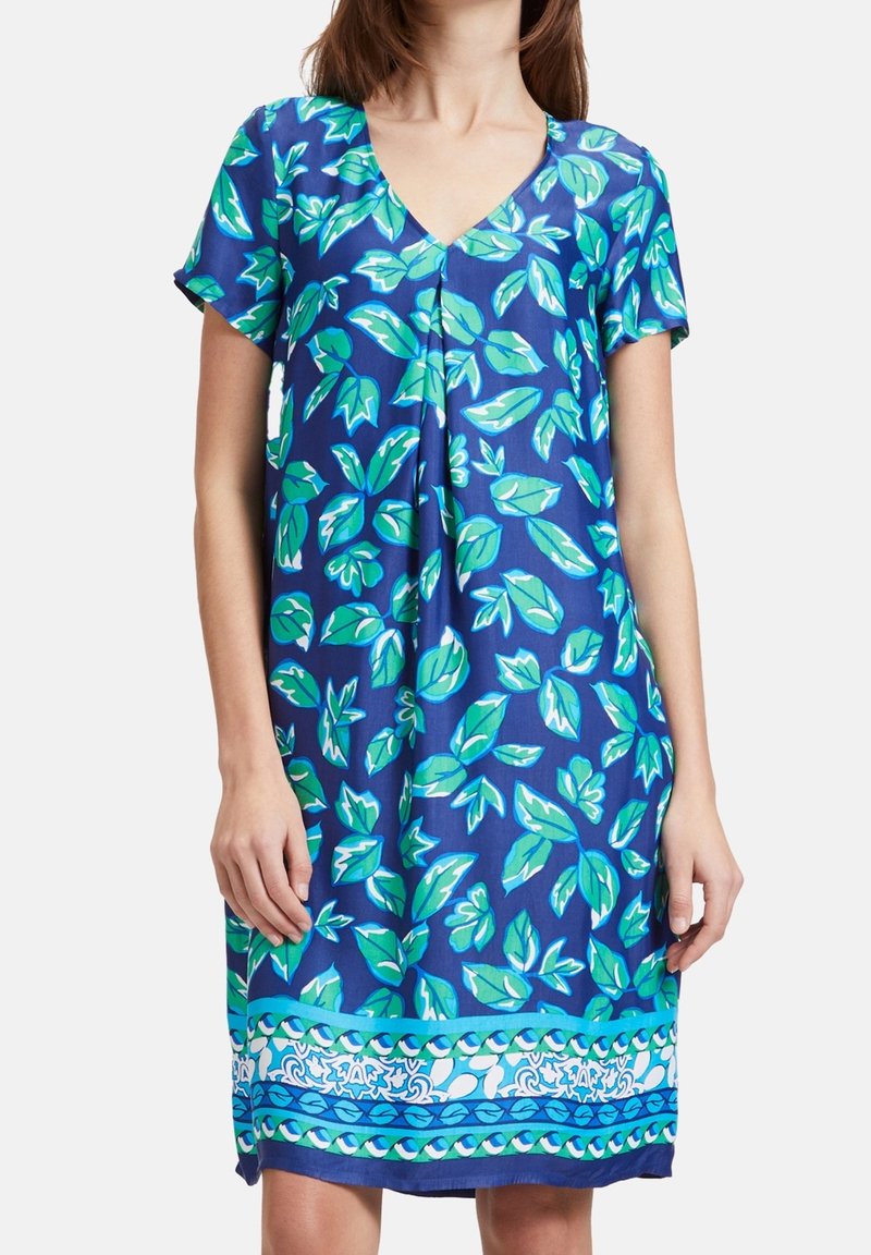 Vestido de manga corta en tela azul con patrones de hojas verdes, escote en V y una banda decorativa cerca del dobladillo en blanco y azul.