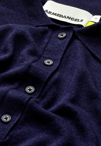 Marineblaues Polohemd aus strukturiertem Stoff, mit einer Dreiknopfleiste mit runden Knöpfen und einem Markenetikett am Kragen.