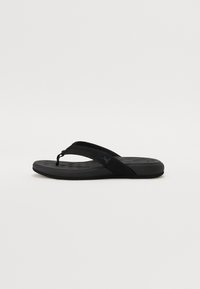 Black flip-flop sandal with textured fabric straps and cushioned sole, featuring a curved shape and subtle branding on the strap.