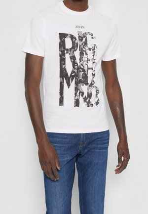 Vit bomull t-shirt med stor svart grafisk text som består av kollagerade bilder. Matchad med blå denimjeans för kontrast.