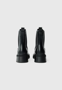 Botas de tobillo de cuero negro con paneles laterales elásticos y lengüetas. Suelas de goma gruesas y texturizadas que proporcionan tracción y estabilidad.