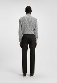 Black trousers paired with a light blue striped long-sleeve shirt. Visible stitching, button details, and a classic collar are notable features.