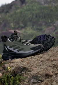 Black and olive green hiking shoes with textured fabric upper, rubber sole, and sturdy lace-up design. Features purple accents on the sole.