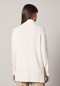 Cremfarbener Pullover mit hohem Kragen, geripptem Saum und langen Ärmeln. Weicher Stoff, lockere Passform und verlängertes Rückendesign.