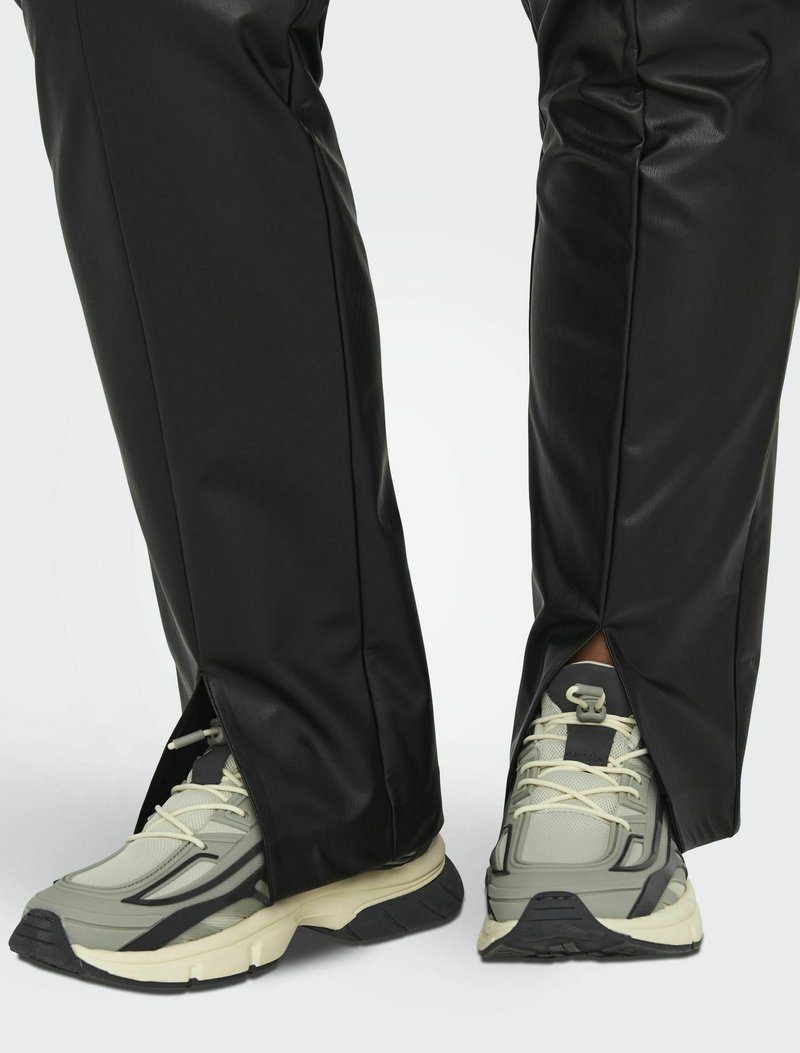 Zwarte faux leren broeken met zijritsen, gecombineerd met grijze en crèmekleurige sneakers met een textuuroverleg en veters.