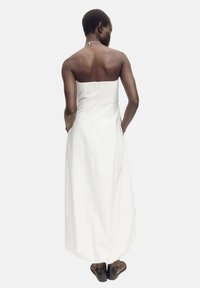 Robe maxi blanche sans bretelles avec un buste ajusté, une jupe évasée et des poches latérales. Texture lisse et design simple et élégant.