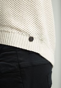 Strickpullover in Off-White, mit strukturiertem Design und geripptem Saum. Enthält ein kleines, dunkles Metallelement an der Seite.