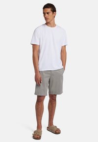 T-shirt bianco in cotone, pantaloni corti grigio chiaro e sandali slip-on color beige. Design semplice, vestibilità rilassata e texture uniformi. Nessun motivo o accento.