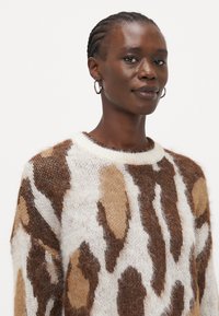 Brown and cream patterned sweater made of soft, textured knit, featuring a crew neckline and a relaxed fit with distinct abstract shapes.