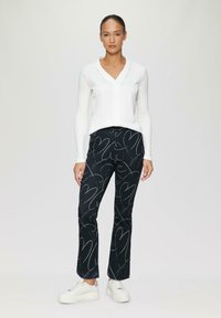 Witte lange mouwen shirt met een V-hals, gecombineerd met zwarte broek met een hartpatroon in het wit en dikke witte sneakers.