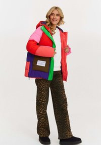 Farebná prešívaná bunda so sekciami v červenej, ružovej, zelenej a fialovej farbe, s kapucňou a predným zipsom. V kombinácii s nohavicami s leopardím motívom.