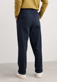 Pantaloni de culoare albastru marin cu talie elastică, cu manșete răsucite, confecționați din bumbac. Au o buzunare la spate și o textură moale. Purtați cu pantofi albi.