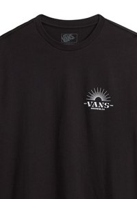 Camiseta de algodón negra con cuello redondo, que presenta un logo de Vans blanco y un gráfico de explosión solar en la parte izquierda del pecho. Textura suave.