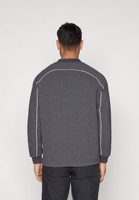 Γκρι μακρυμάνικη μπλούζα με λευκή ραφή κατά μήκος των ραφών των ώμων, κατασκευασμένη από υφασμάτινη υφή, με στρογγυλή λαιμόκοψη και ριμπ μανσέτες.