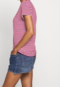 Czerwono-biała koszulka w paski z krótkim rękawem i okrągłym dekoltem, w połączeniu z postrzępionymi szortami dżinsowymi, prezentująca swobodny styl.
