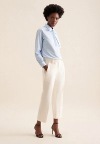 Light blue long-sleeve shirt with a tie collar, paired with white tailored trousers and black high-heeled sandals. Smooth, polished fabric.