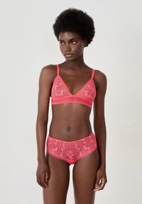 Bralette de encaje rosa con copas triangulares y bordes festoneados, combinado con unas braguitas altas a juego con estampados florales y un acabado de encaje.