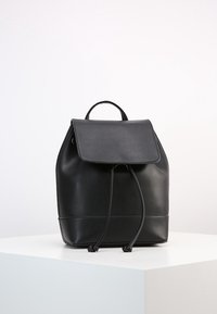 Sac à dos en cuir noir avec une fermeture à cordon, forme structurée, grande rabat avant et une poignée supérieure. Texture lisse avec un minimum de détails.