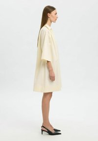 Vestido camisero de gran tamaño color crema con mangas cortas, cuello tipo solapa y dobladillo recto. Combinado con tacones negros de tipo slingback.