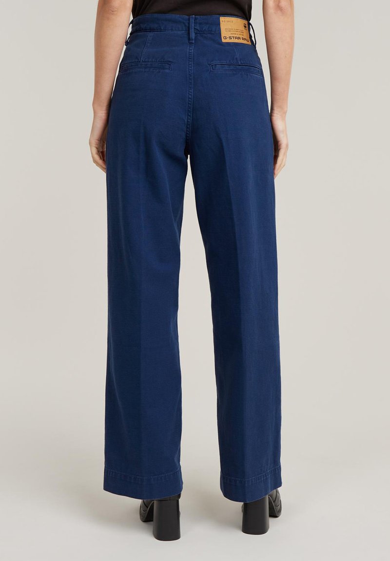 Granatowe spodnie o szerokich nogawkach wykonane z bawełny, z gładką fakturą, z metką marki z tyłu oraz dwiema tylkami kieszeniami.