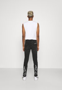 Black denim jeans with flame pattern printed in white on the legs, paired with a sleeveless white top and white sneakers.