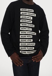 Maglietta nera a maniche lunghe con frasi in bianco in stile ritagliato, caratterizzata da una vestibilità comoda e scollatura rotonda.