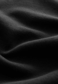 Gros plan sur un tissu noir doux et lisse avec des plis subtils et une texture tissée fine sous un éclairage doux.