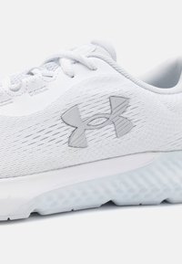 Zapatilla deportiva blanca con una parte superior texturizada, que presenta un logo gris, malla ligera y una suela ligera y estampada para tracción.