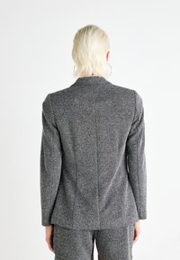 Gråtexturerad blazer med långa ärmar, figursydd design och lätt axelp padding. Har en ren bakseam och slagkrage.