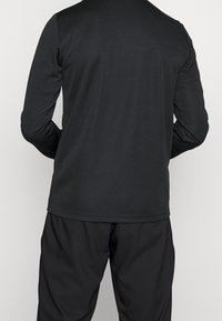 Schwarzes Langarmshirt mit Rundhalsausschnitt, glatter Textur und lockerer Passform, kombiniert mit passenden schwarzen Hosen.