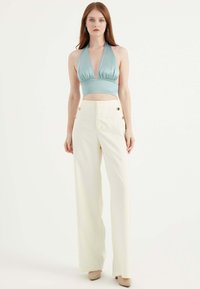 Ljusblå halterneck crop top med en rynkad midja, parat med högmidjade, krämfärgade vida byxor med guldknappdetaljer.