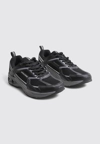 Baskets noires en mesh et en matériaux synthétiques. Elles comportent des lacets, un col rembourré et des accents réfléchissants sur les côtés.