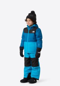 Modro-čierna izolovaná zimná bunda s rovnako ladenými nohavicami, textúrovanými rukavicami a pletenou čiapkou s brmbolcom a vzorom vločiek.