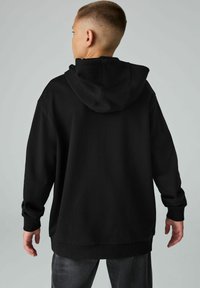 Sudadera con capucha negra de corte relajado, con puños y dobladillo de canalé. Está hecha de una tela texturizada. Incluye una capucha amplia y un detalle de costura en la parte trasera.