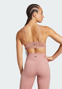 Sujetador deportivo rosa con múltiples tirantes estrechos y un logotipo de marca, combinado con leggings rosa de cintura alta con un logotipo en la parte trasera.
