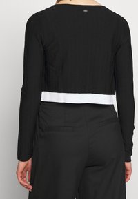Top corto negro de manga larga con textura acanalada, detalle de dobladillo blanco y escote rectangular. Tejido suave con ligero brillo.