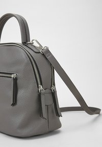 Harmaa nahkareiho, jossa on kivetty pinta, kaksinkertaiset vetoketjut ja etutasku. Varustettu säädettävällä olkahihnalla ja yläkahvalla.