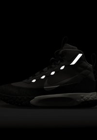 Melna sporta kurpe ar teksturētu zoli, atstarojošiem akcentiem un augstu dizainu. Iekļauj izteiktu Nike logotipu un sarežģītu šuvumu.