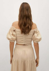 Top beige sin mangas con mangas abullonadas, que presenta un respaldo fruncido y un diseño corto, combinado con una falda a juego con volantes.