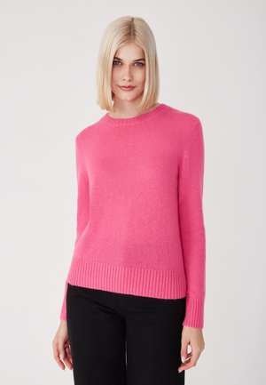 Rosa gestrickter Pullover mit Rundhalsausschnitt, geripptem Saum und Bündchen, der eine weiche Textur aufweist. Tragen mit schwarzen Hosen.