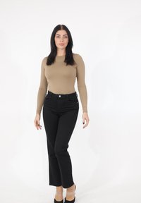 Haut beige à manches longues, jean noir taille haute, chaussures à talons transparents. Design simple, coupe ajustée, texture lisse et palette de couleurs monochrome.