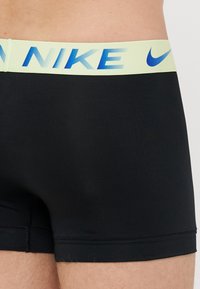 Crne gaće uskog kroja, s svijetložutim pojasom na kojem se nalazi plavi "Nike" logo i glatkom, rastezljivom tkaninom.