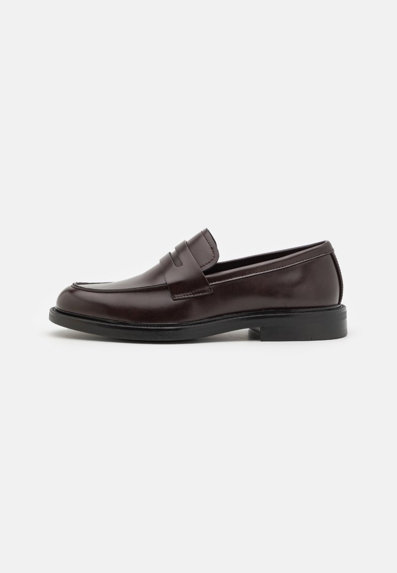 Mocassin penny en cuir marron foncé avec semelle noire et petit talon, présenté du côté intérieur sur fond blanc.