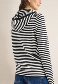 Zwart-wit gestreepte hoodie, met een zachte textuur, geribbelde afwerking en een capuchon met trekkoord, gecombineerd met spijkerbroek.