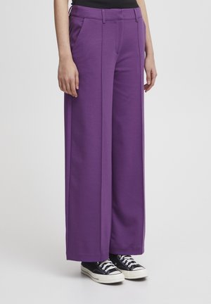 Pantalons larges violets en tissu doux, dotés de poches avant et d'une texture lisse, associés à des baskets basses noires.